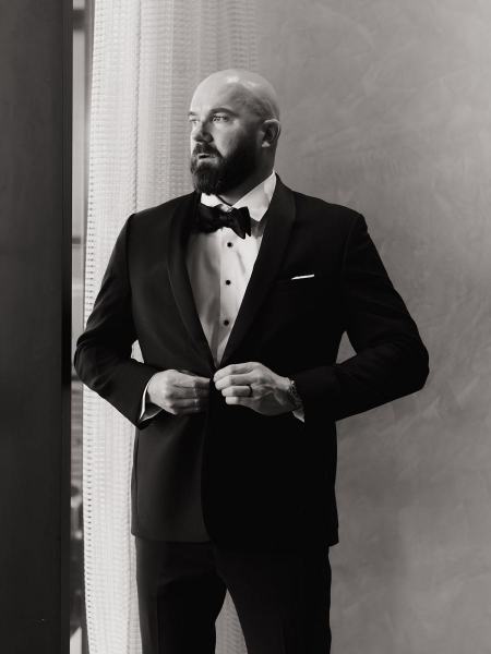 Groom adjusting tie while groomsmen prepare in suite at The Ben Autograph Collection Hotel Palm Beach